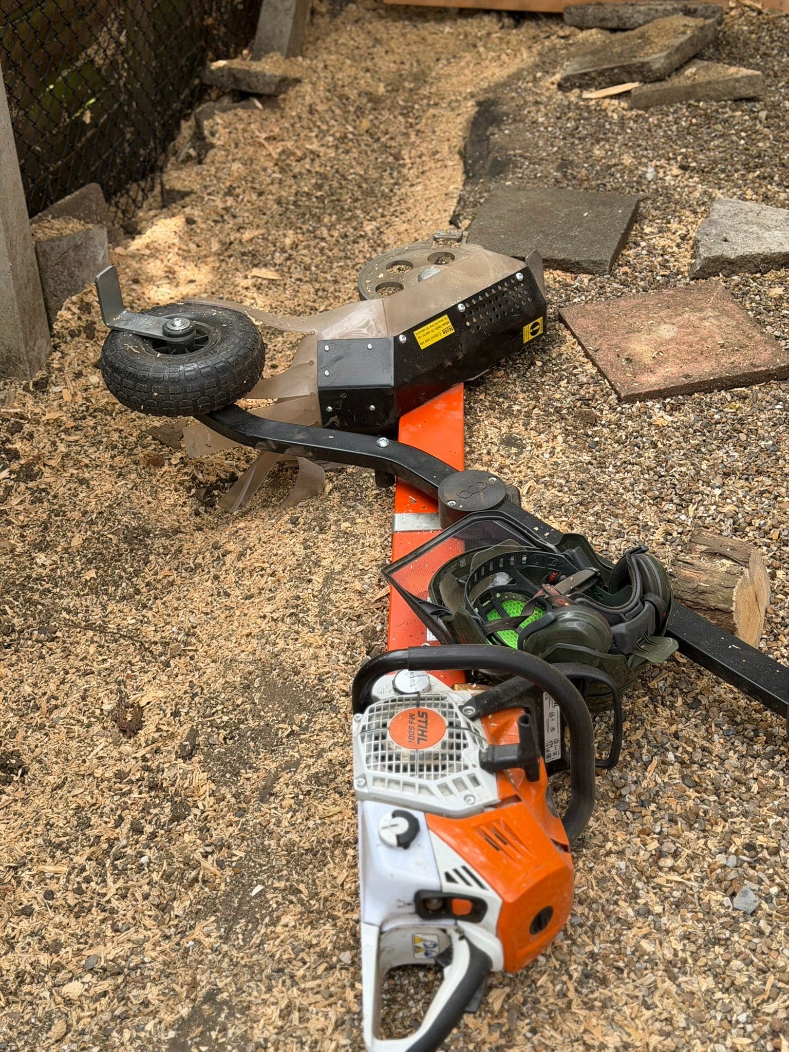 The Terminator stump grinder attachment fitted to a Stihl MS 500i chainsaw, with its cutting wheel, guard and single transport wheel, lying on wood chippings