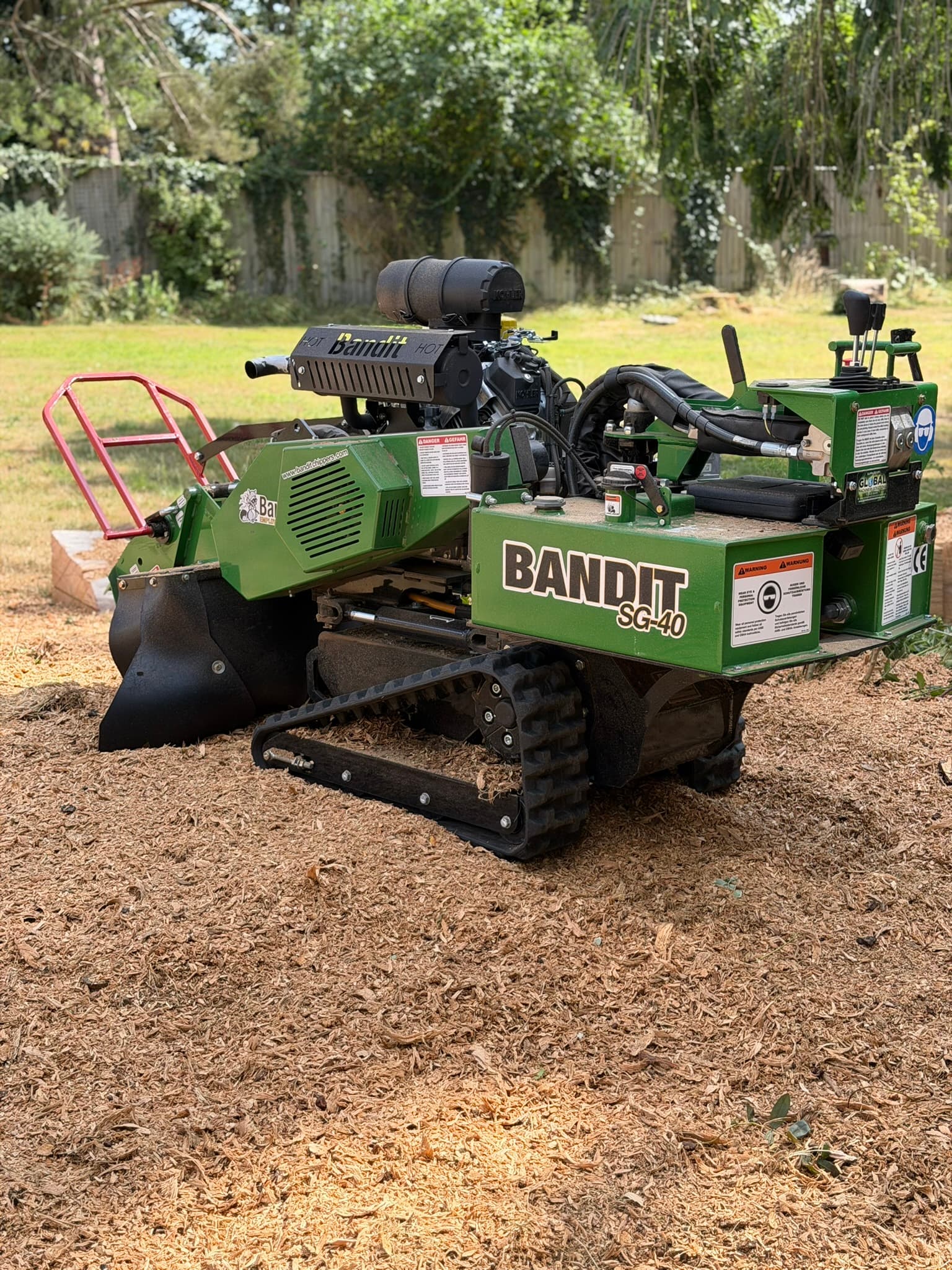 The cleared area after grinding, now a bed of fresh wood chippings where the cedar stump used to be, with the Bandit SG-40 grinder parked on it