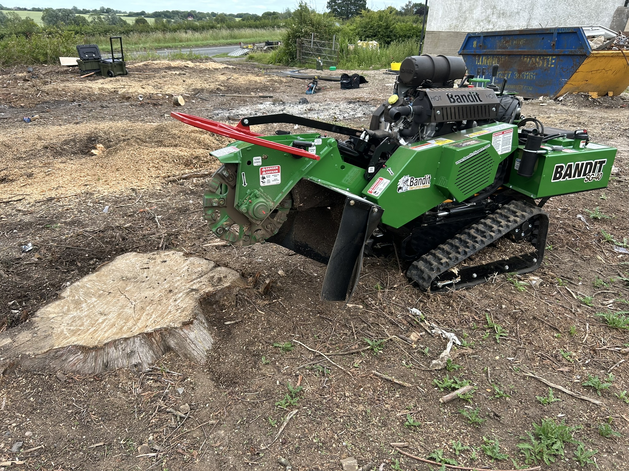 A Bandit SG-40 tracked stump grinder positioned beside a large freshly cut tree stump on an open site, with wood grindings on the ground