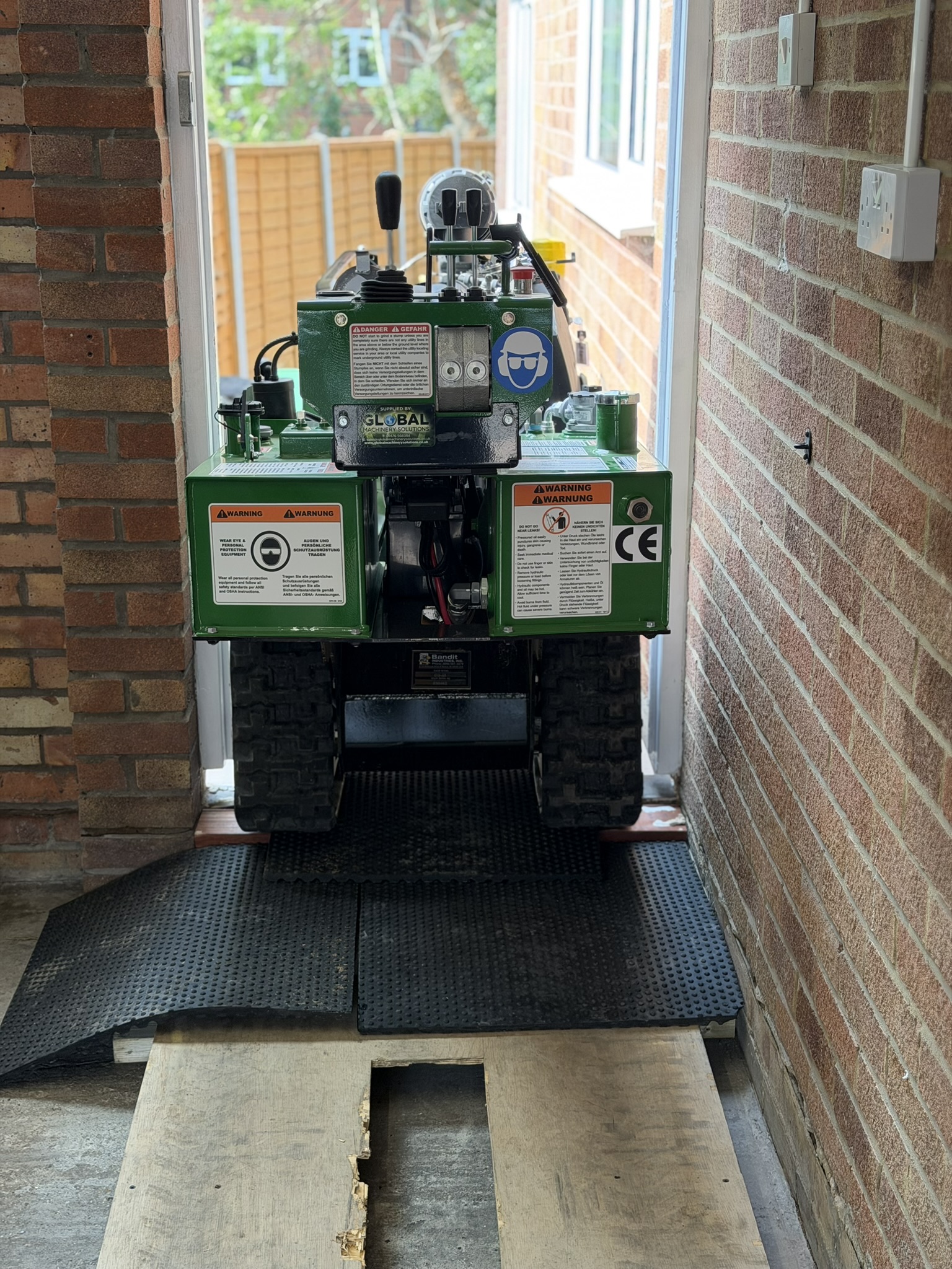 A green Bandit SG-40 tracked stump grinder driven through a narrow doorway on mats and boards, showing the restricted access
